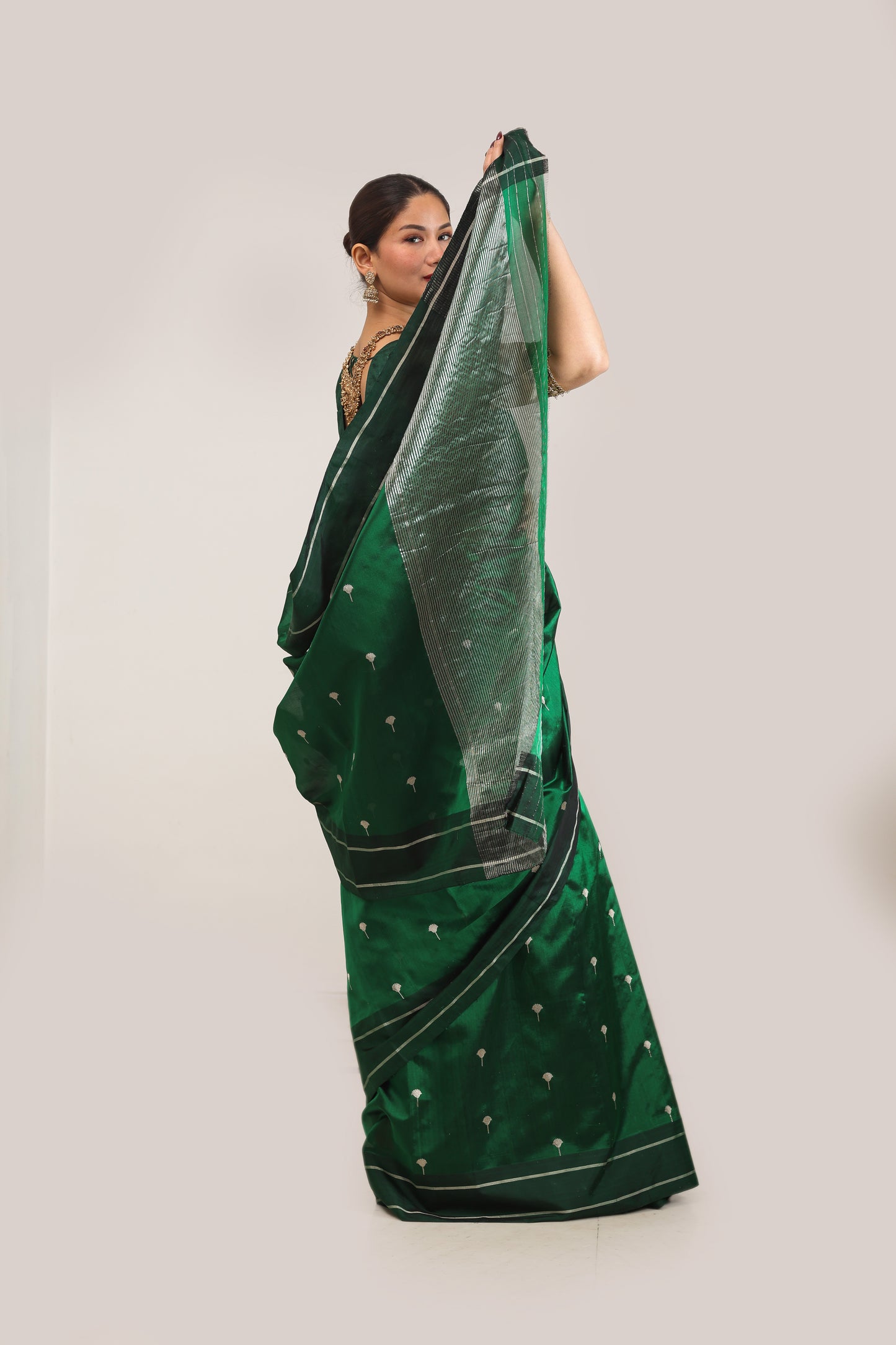 Woman wearing a green saree with a white border on a light gray background