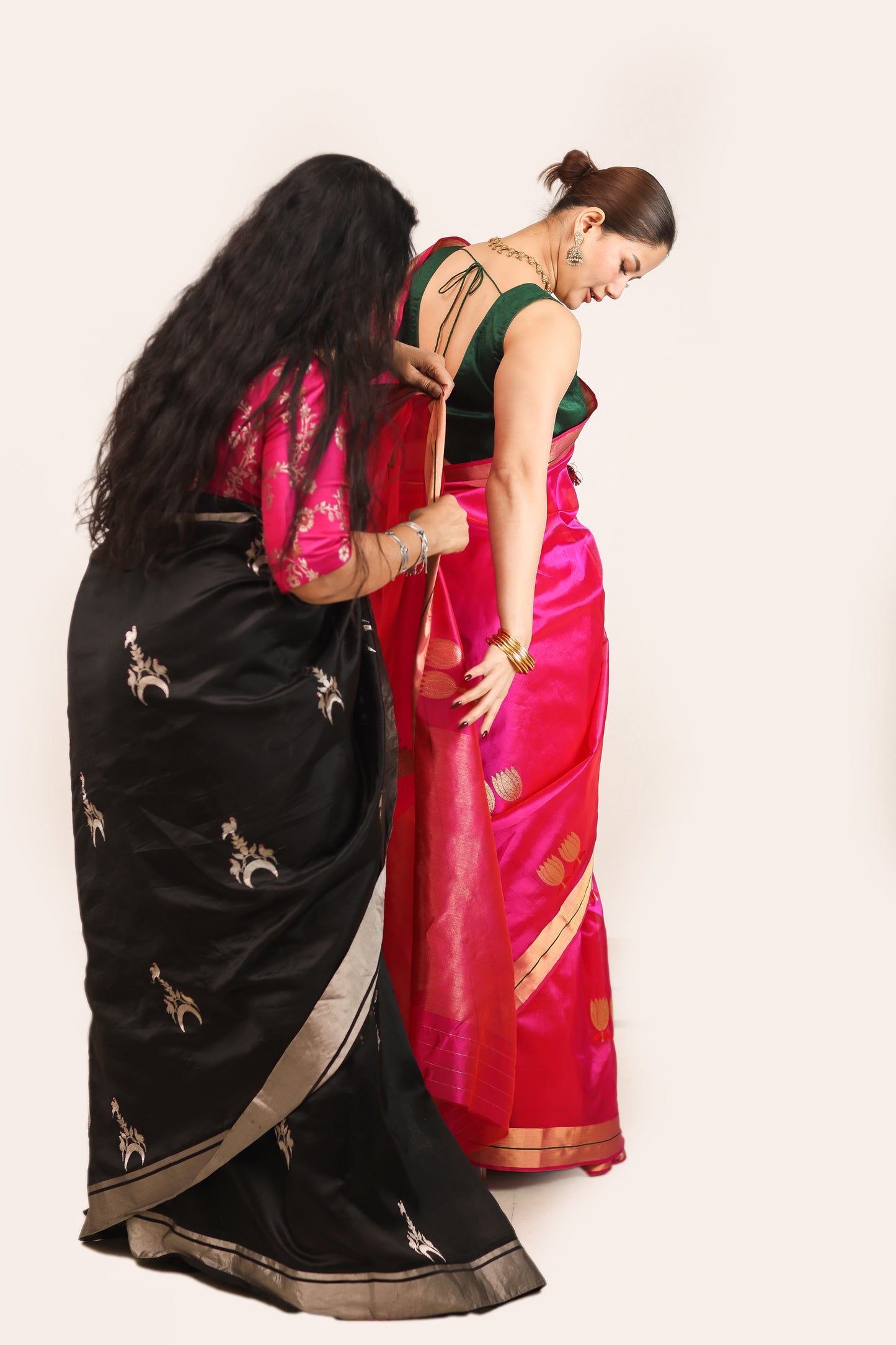 Two women wearing traditional sarees against a plain background